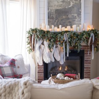 Collection of white stockings hung by a cozy fireplace draped in greens, red bells, and ribbons