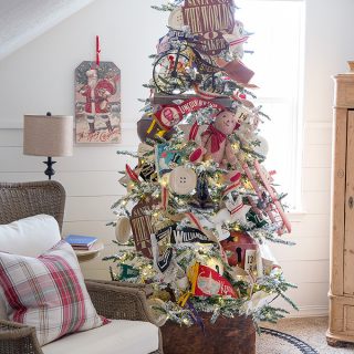 A flocked Christmas tree decorated with vintage toys, pennant banners, grain sack accents, and bells.