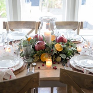 A simple DIY Christmas centerpiece with fresh greenery, oranges and pomegranates, and the soft glow of candlelight