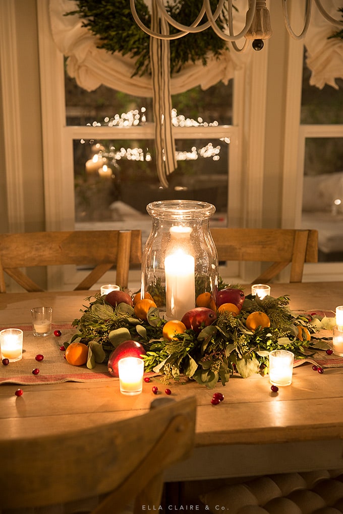 Red pears, oranges, and cranberries accent this easy DIY candle ring centerpiece in the warm glow of candlelight