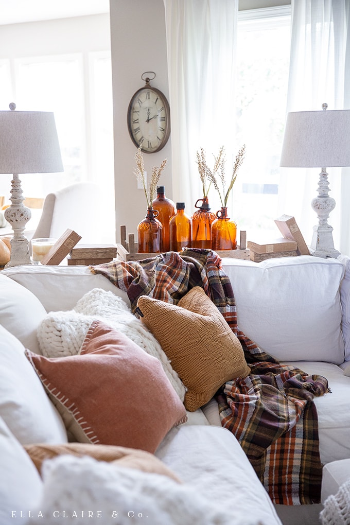 A cozy, rustic family room decorated for fall with touches of plaid, vintage amber glass, wood tones, and other antique elements,elements, enhanced with so much texture through blankets, throws and pillows. 